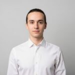 Mladý dospělý v bílé košili stojící před šedým pozadím s neutrálním výrazem obličeje