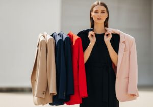 Stylová žena v černých šatech s různobarevnými saky na ramenou na neutrálním pozadí